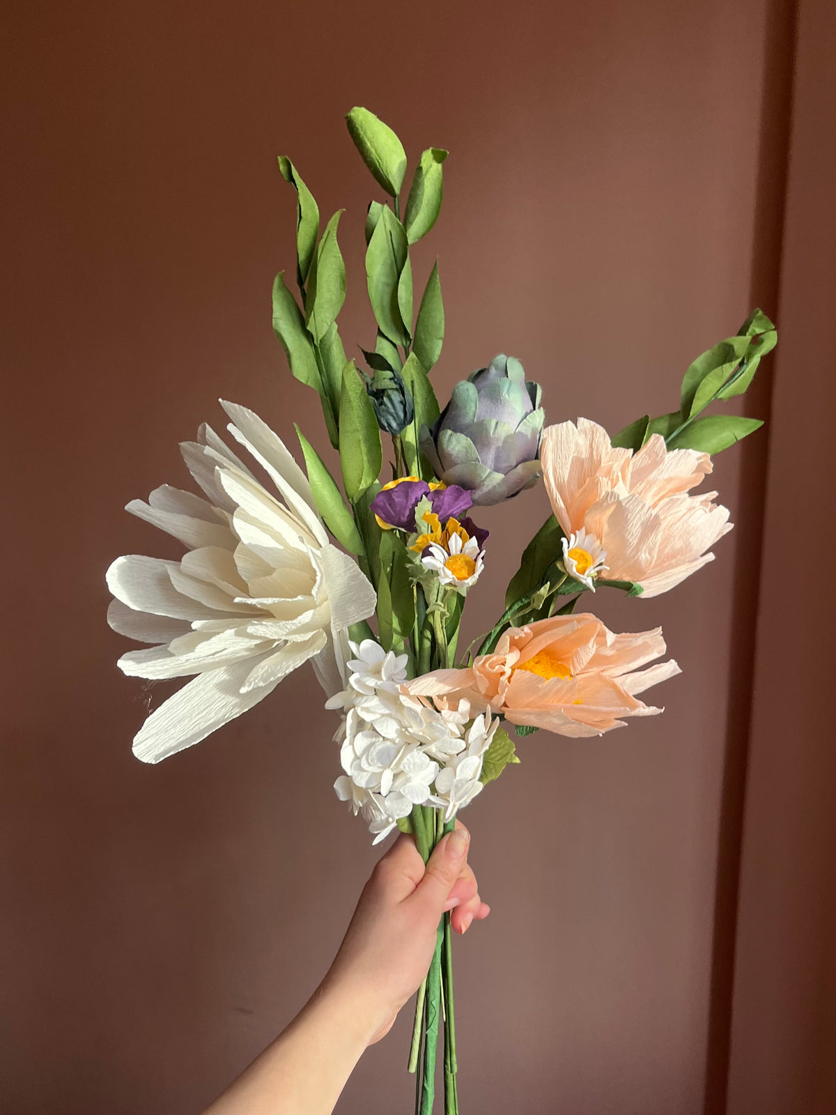 Evighedsbuket af papir i fersken og hvid med artiskok, tusindfryd og hortensia mod brun væg