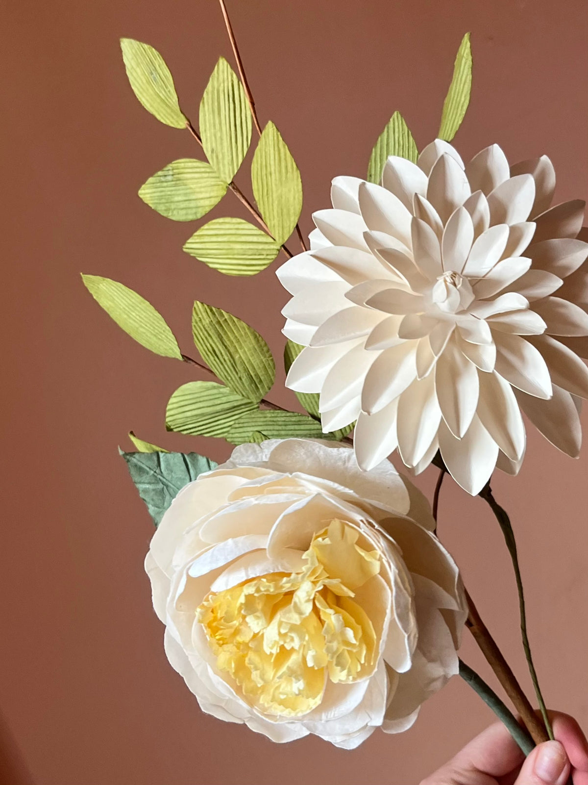 Nærbillede af creme dahlia og rose med gult hjerte i papir med lysegrønne grene