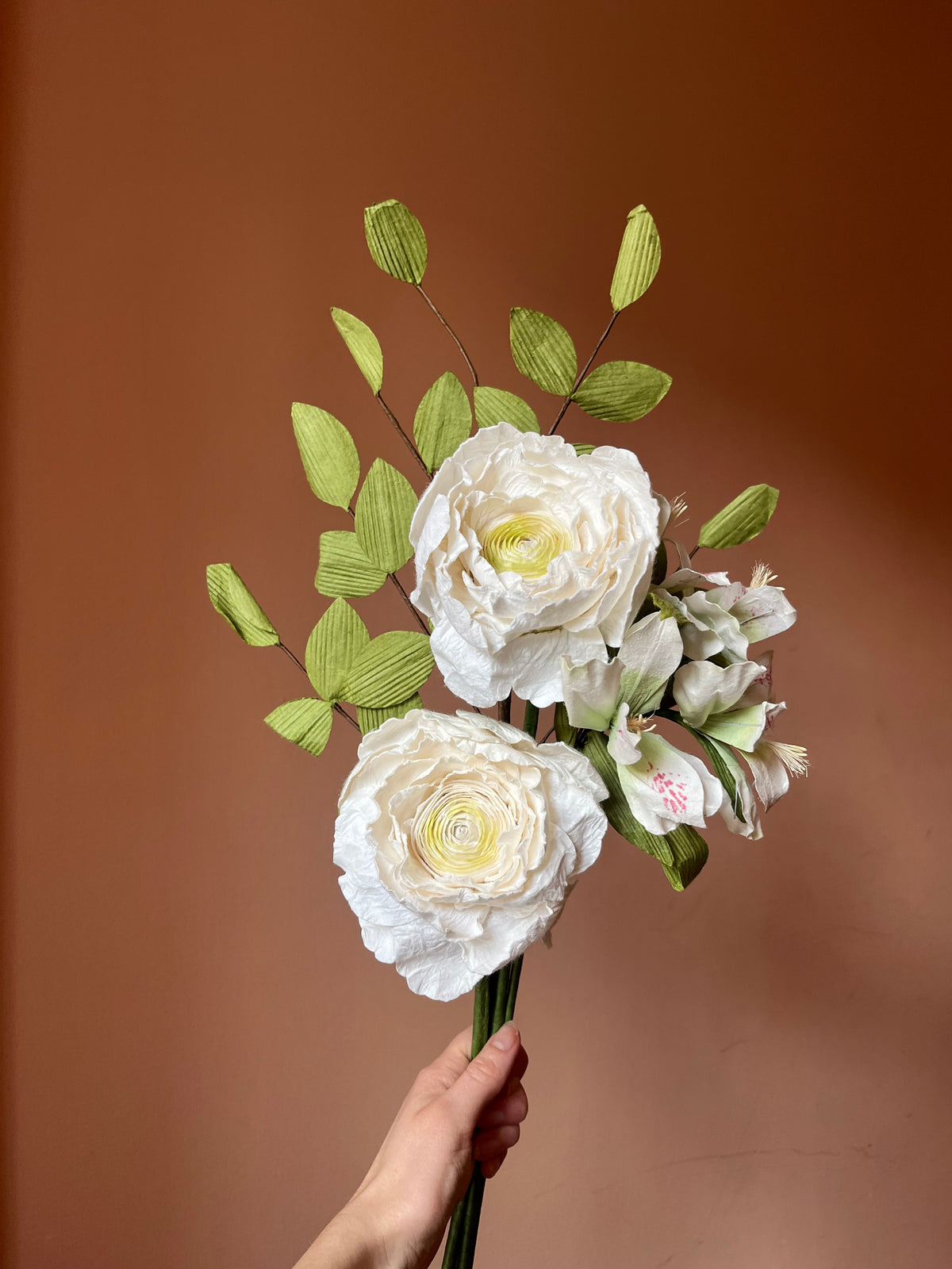 Hånd holder hvid evighedsbuket af papirblomster med ranunkler og lysegrønne grene