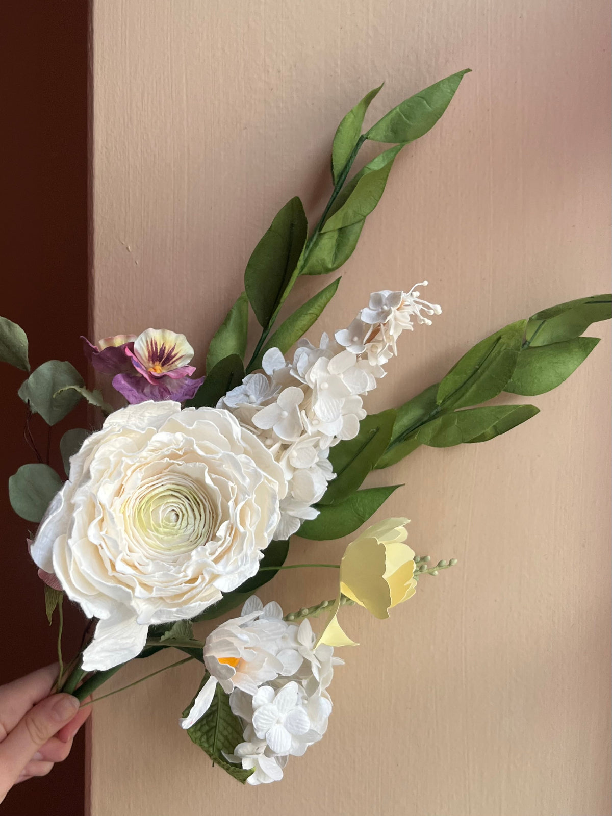 Hvid evighedsbuket af papir med ranunkel, hortensia og eukalyptus mod lyserød væg