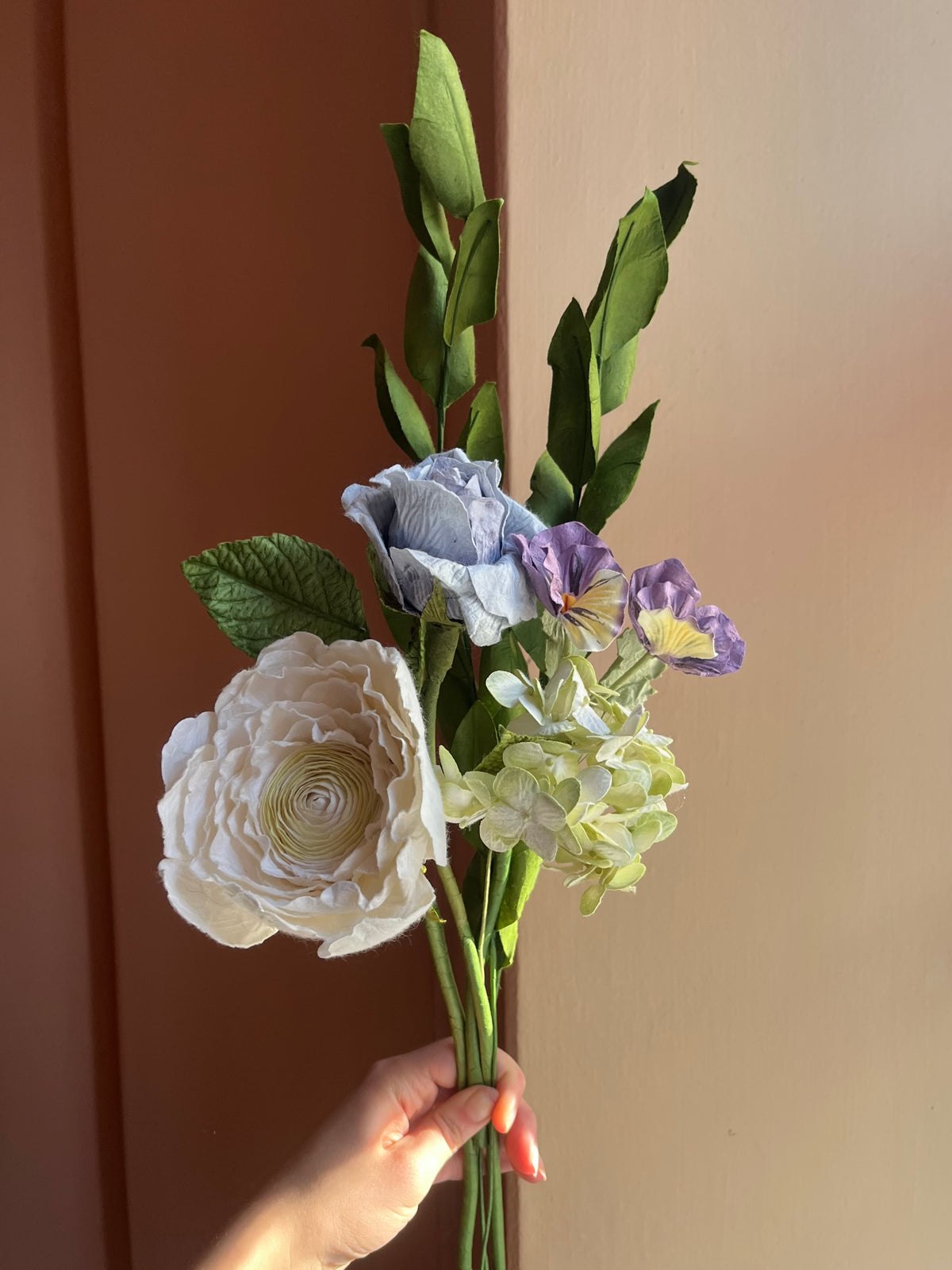 Hånd holder evighedsbuket af papirblomster i hvid, blå og lilla